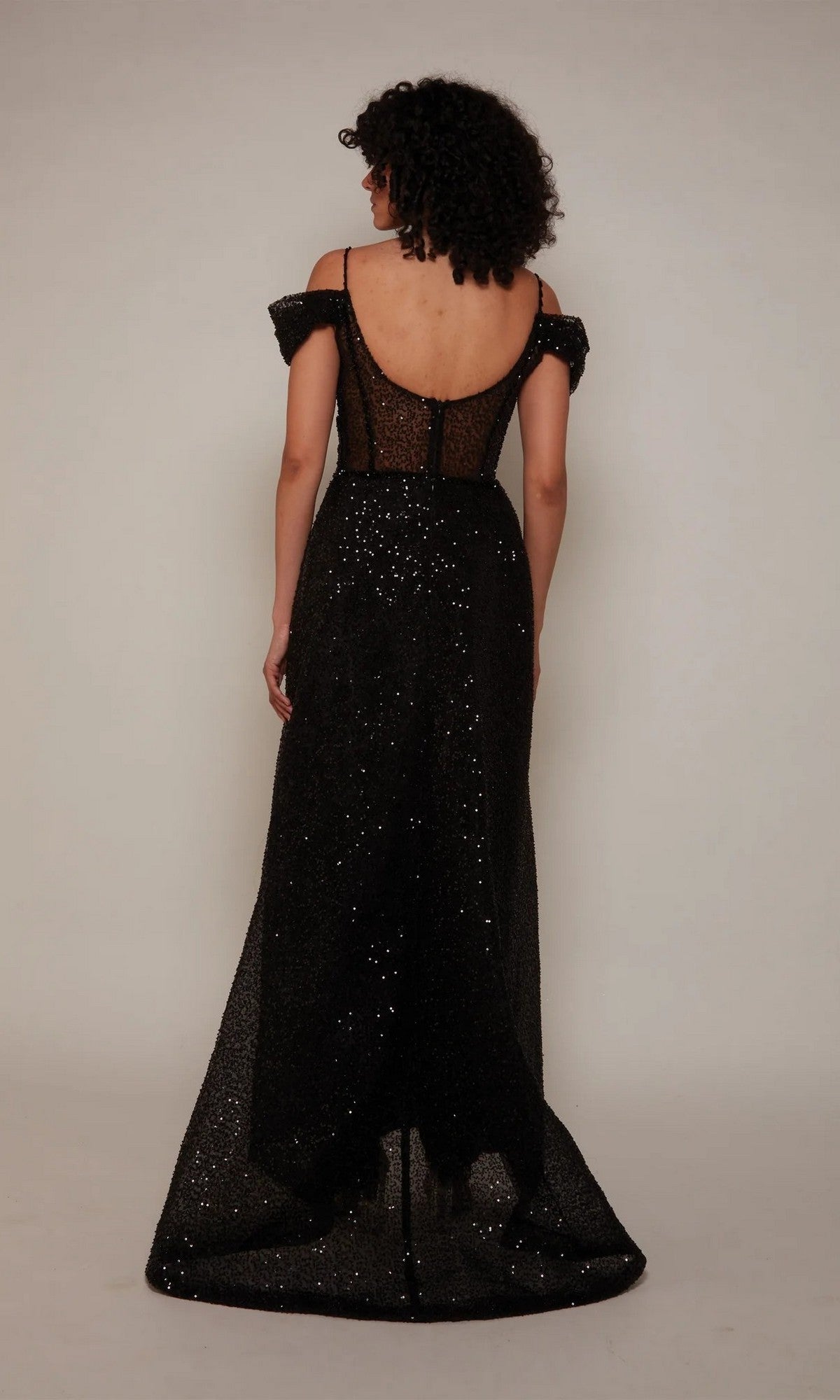A person with curly hair is wearing the Alyce 7101 long formal dress, featuring an off-the-shoulder design, floor-length glitter fabric, and a sheer back, standing against a plain light background.